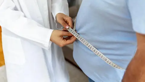 Getty Images Doctor measures a man's waistline during a clinic check