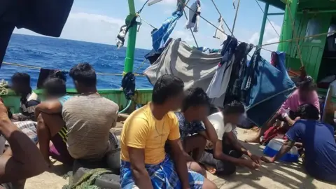 Handout The Tamil migrants, with their faces blurred or turned away from the camera, sitting on the deck of a boat, with washing on lines around them, as they sailed through the Indian Ocean