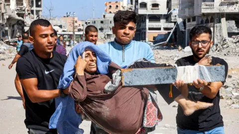 AFP Men carry an injured woman out of Jabalia refugee camp, in the northern Gaza Strip (9 October 2024)