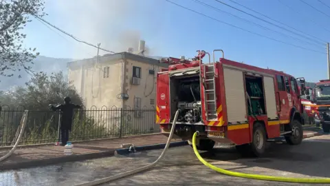 BBC Firefighters put out a blaze at a residential building hit by a Hezbollah rocket in Kiryat Shmona, northern Israel (9 October 2024)