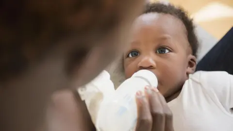 Getty Images A close up of a baby being fed from a bottle by its mother