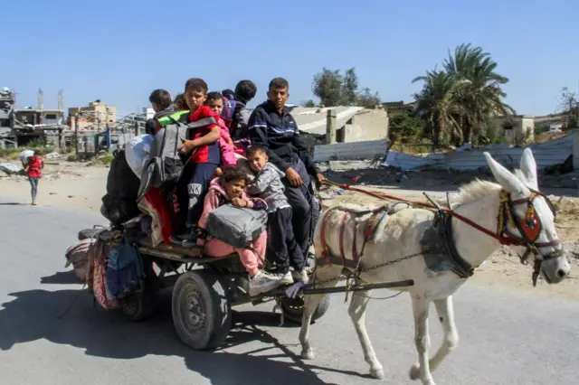 A cart pulled by a donkey, stacked with bags and people including children sitting on top of it