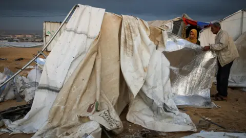 Reuters Displaced Palestinians inspect damage to their tent after an Israeli strike, in the al-Mawasi area, in the southern Gaza Strip (15 October 2024)