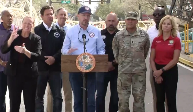 Kevin Guthrie standing at a lectern speaking, he is surrounded by people