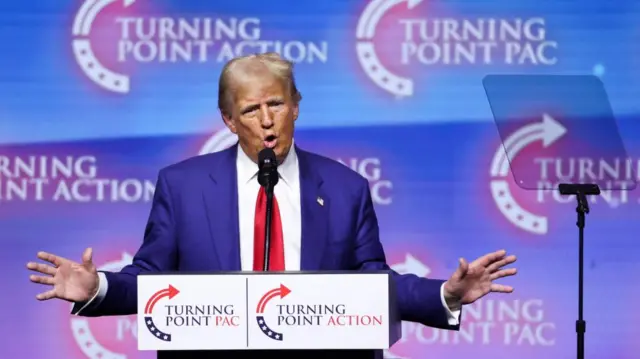 Donald Trump stands at a podium during a Turning Point rally