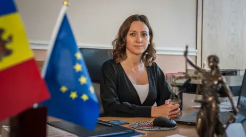 Matthew Goddard Moldova’s chief anti-corruption prosecutor Veronica Dragalin sat in her office at her desk. Visible in the image is a flag of Moldova and a flag of the EU.