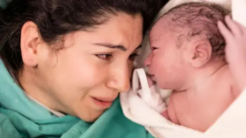 Getty Images Mother lying down and cradling her newborn baby in hospital