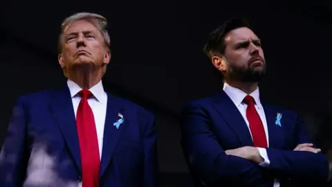 AFP Donald Trump and JD Vance stand side-by-side, wearing navy suits and red ties. Trump has fair hair and has a serious expression on his face. Vance has brown hair and a beard, and looks quizzical.