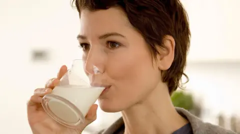 Getty Images A woman with short brown hair drinks milk from a glass which is at her lips