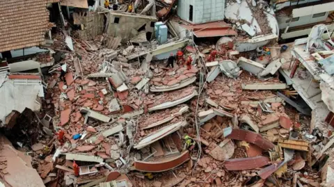 Reuters / Pablo Funes Aerial drone photograph shows the widespread debris and damage from the hotel collapse from a bird's eye view. Rescue workers can be seen scaling the debris with a range of apparatus and emergency workwear.