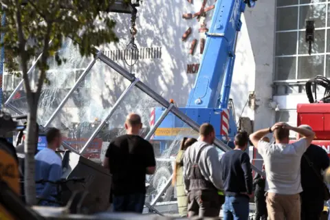 AFP via Getty Images Men stand in front of a crane and a smashed glass structure outside a railway station in Serbia