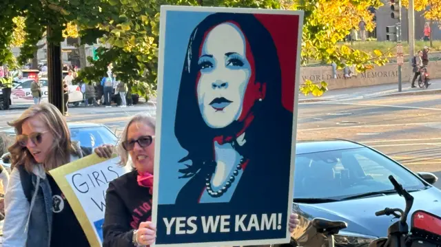 Marcher holds up poster with Kamala Harris's face and slogan 'Yes we Kam!"