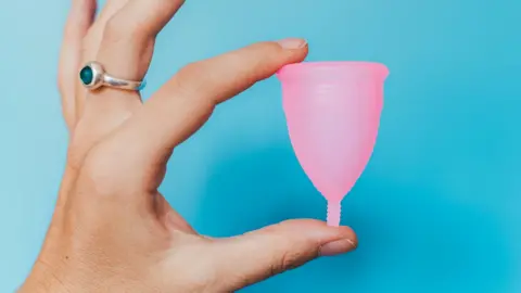 Getty Images A woman's hand holding a menstrual cup between her thumb and finger