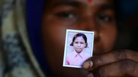 Getty Images An Indian woman in blurred focus holds out a small photo of her daughter who died of Guillain Barre Syndrome during an outbreak in 2019