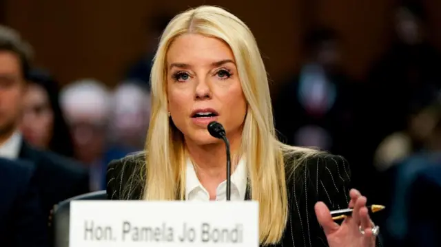 Bondi, seated, speaks into a microphone, as people sitting behind her look on