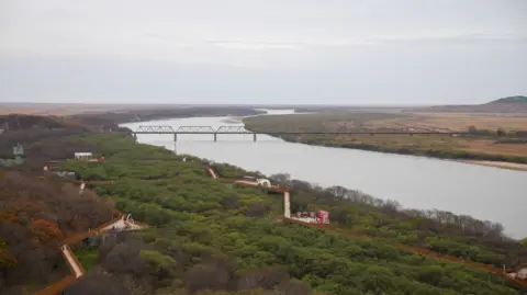 The friendship bridge connecting Russia and North Korea over a grey winding river.