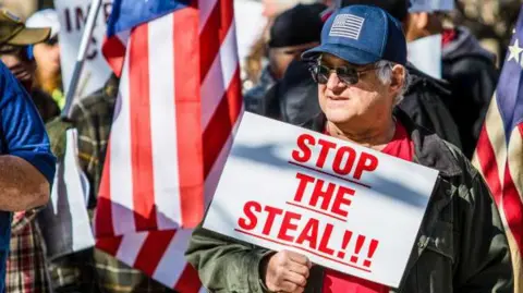 Getty Images A protester wearing a baseball cap with an American flag on it holds a placard reading "Stop the Steal"