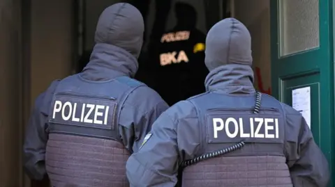 Reuters Two German police officers wearing hoods pictured outside a house from behind.