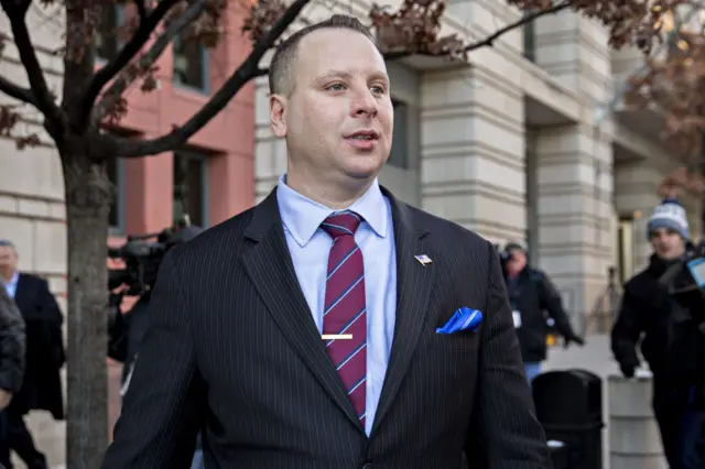 Sam Nunberg walking along a street with reporters behind him in a blurry background