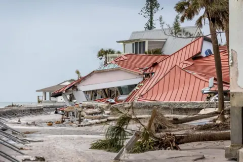 EPA A battered house in the aftermath of a hurricane, there are fallen trees in the foreground.