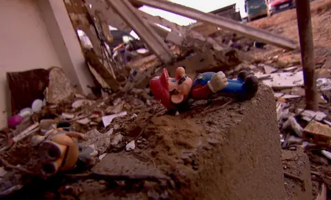 A red and blue Mario plastic toy is sitting on a brick amid a pile of other debris and rubblevcsa