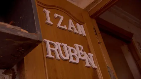 A broken wooden door with white letters spelling out the words "Izan" and "Ruben" nailed onto it