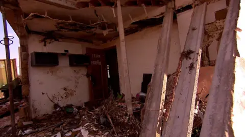 The Matías family house has been largely reduced to rubble, though some walls are still standing. There is debris on the floor and there is a door with the boys' names on that is still standing